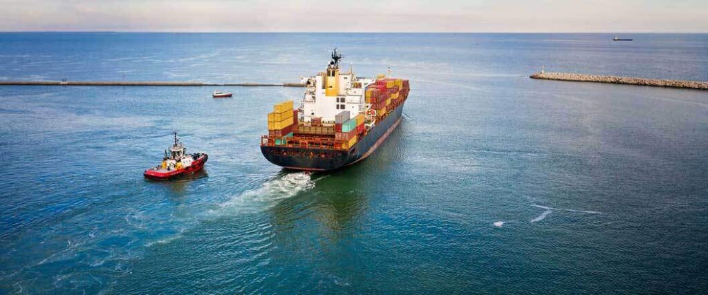 container ship being escorted out of harbor by tugboat