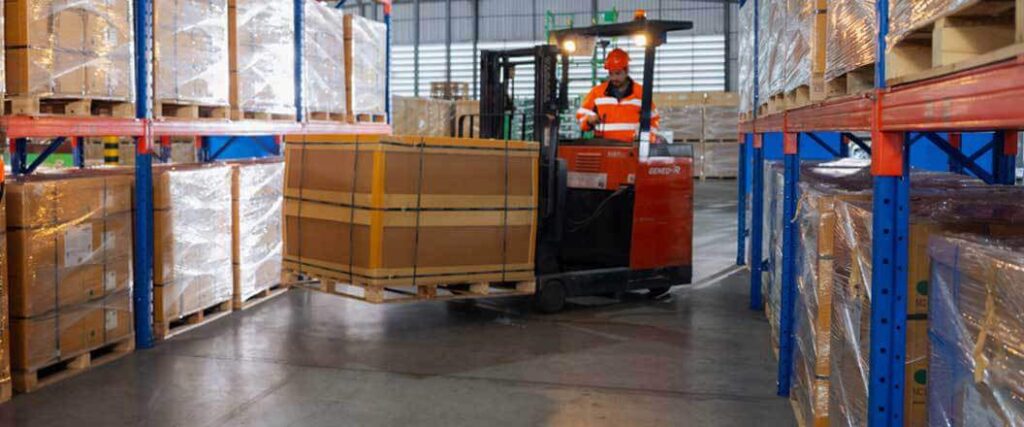 A warehouse worker moving a palletized box with a forklift